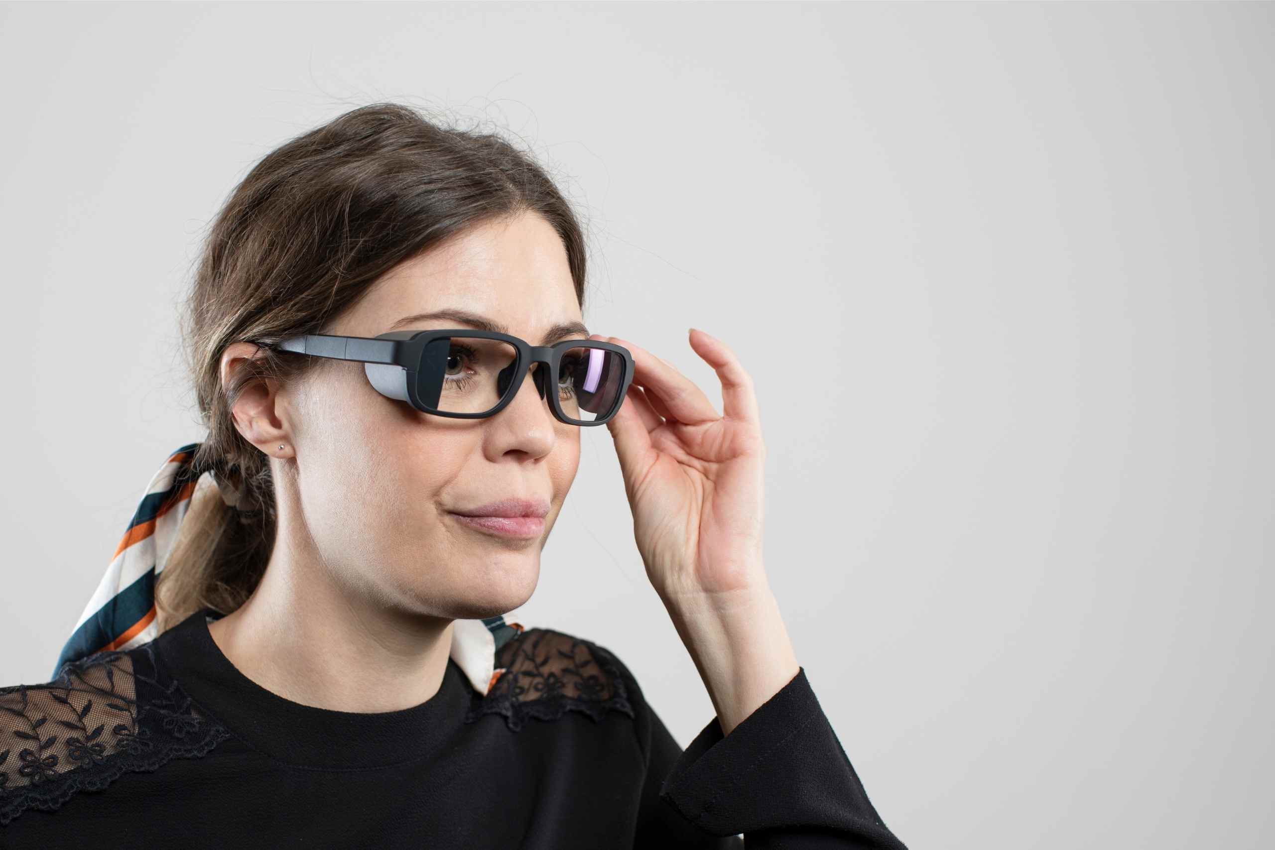 Kvinna som blickar snett framåt rättar till sina brusreducerande glasögon QuietFrames