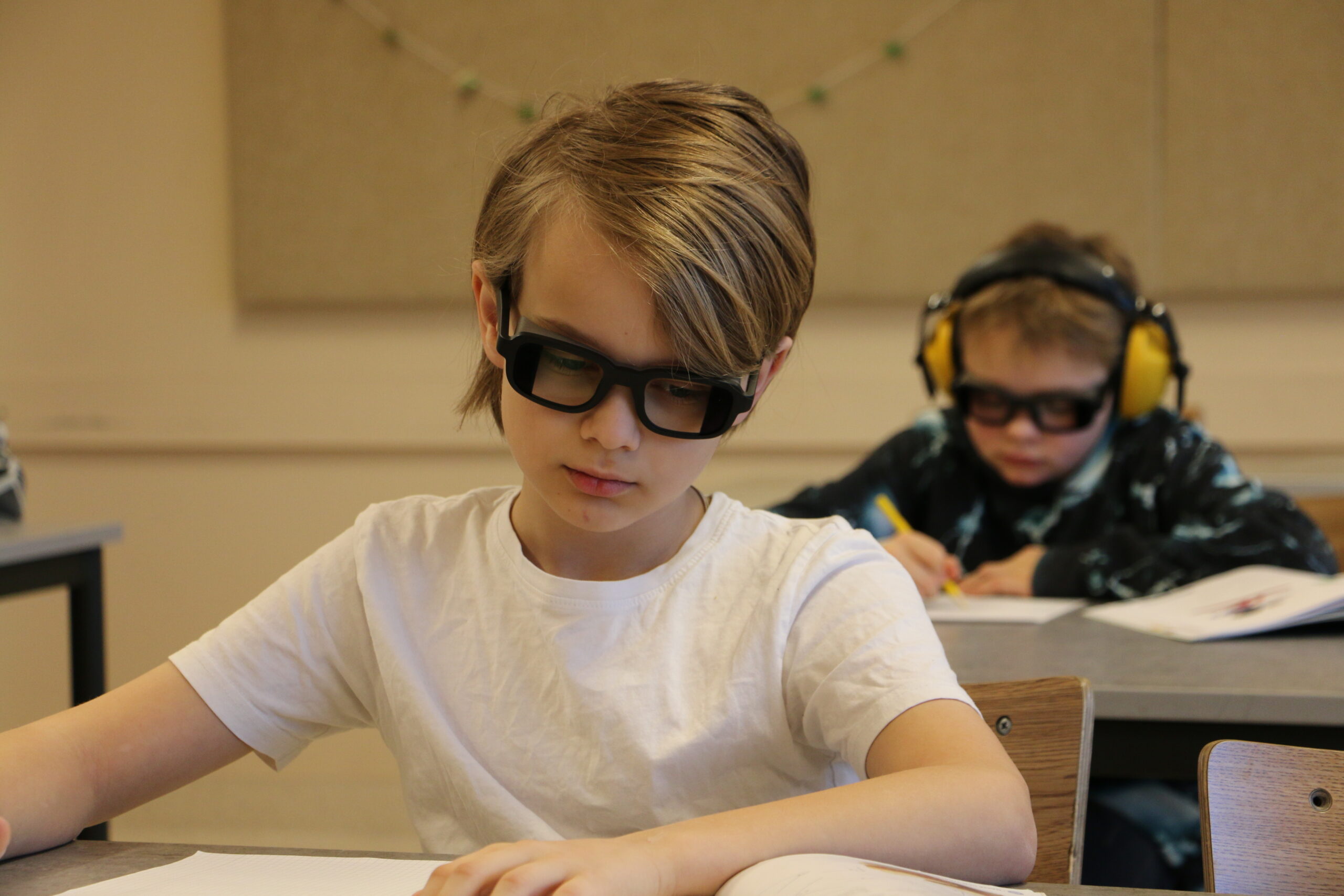Fokuserade elev med QuietFrames sitter framför klasskamrat som har både QuietFrames och hörselkåpor