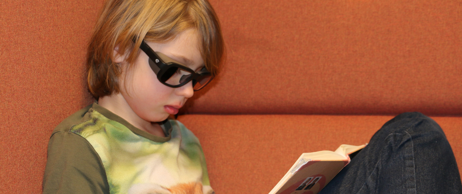 Pojke sitter i en fåtölj och läser fokuserat med sina svarta QuietFrames. Texten handlar om Arbetsminne, koncentration och fokus.